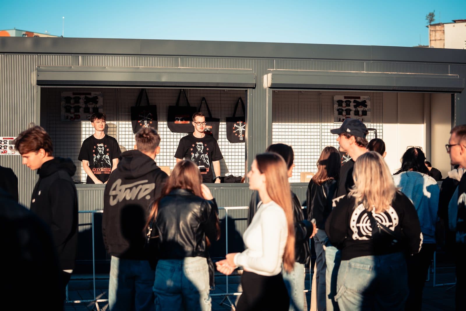 Prodejci Crewmate za pultem merch stánku před O2 arenou na koncertu Yzomandiase, před stánkem fronta fanoušků